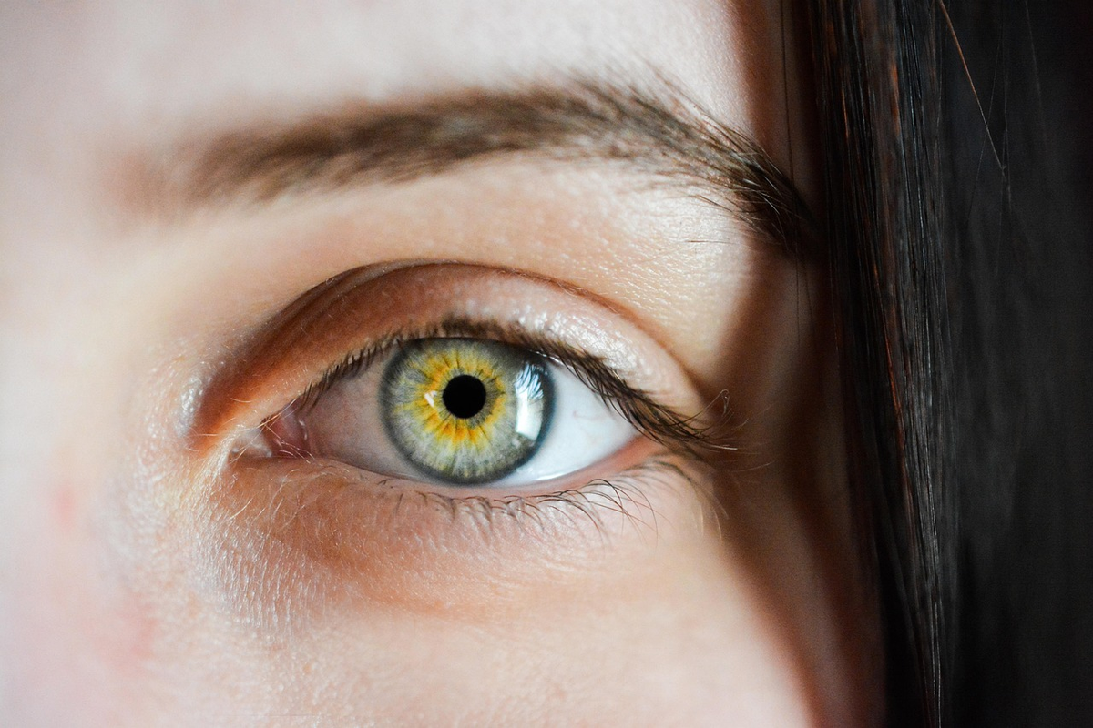 A close-up of a vibrant plate overflowing with fresh, dark leafy greens like kale and spinach, with a subtle golden-yellow glow emanating from them towards a stylized human eye in the background, symbolizing internal nourishment and natural blue light protection for vision.