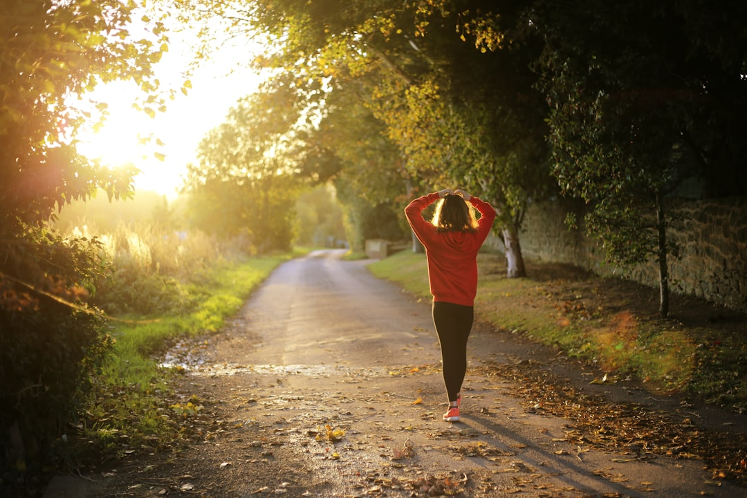 A person in a red hoodie walks along a sunlit autumn country path, embodying a journey toward holistic health and comprehensive well-being.