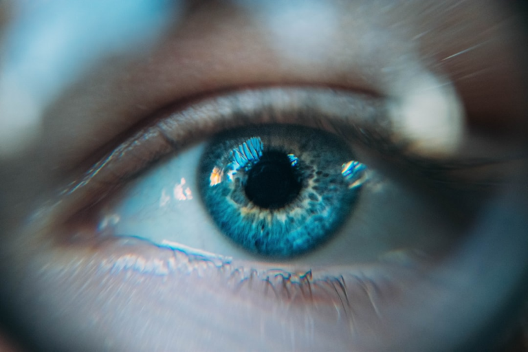 Macro close-up of a striking blue human eye with luminous light reflections on the iris, evoking advanced eye health and biohacking focus.