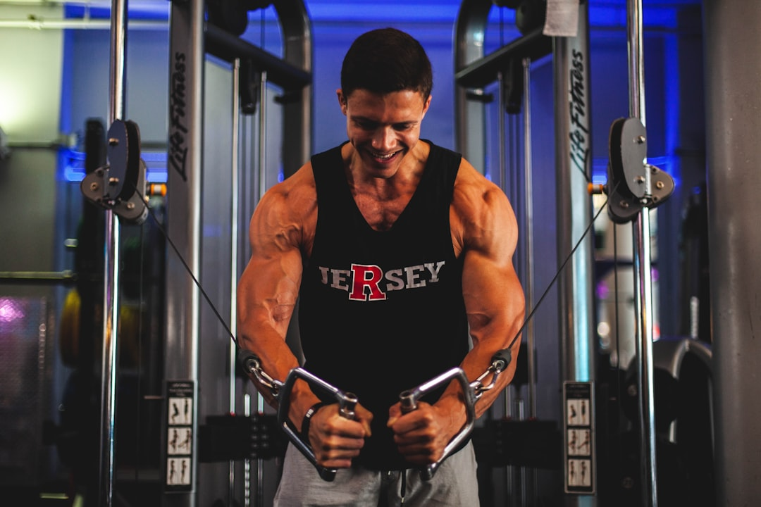 A muscular man with a determined smile performs a cable crossover exercise in a modern gym, showcasing the peak physical energy and strength associated with optimal mitochondrial health.