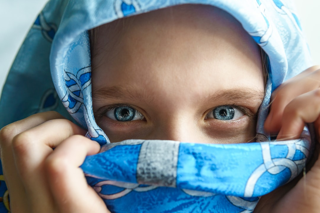 A close-up of strikingly clear blue eyes peeking from behind a bright blue patterned scarf, emphasizing sharp vision and eye health.