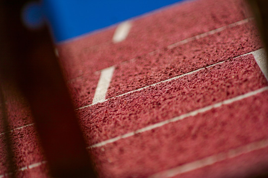 Close-up of a textured red running track with crisp white lane lines under a vibrant blue sky, evoking a sense of forward momentum and the journey towards youthful longevity through hormone optimization.