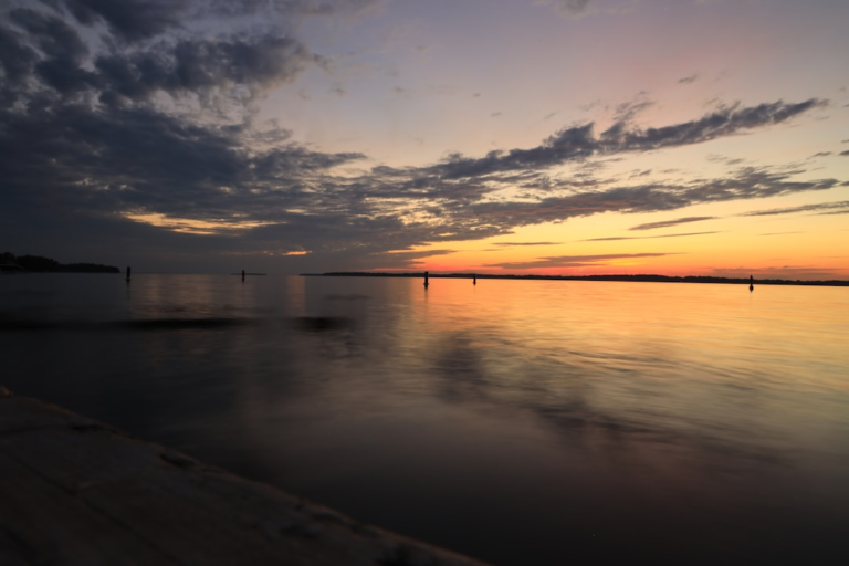Peaceful twilight scene with vibrant orange and purple hues reflecting on calm lake water under a sky of scattered clouds, representing natural light synchronization for circadian rhythms.