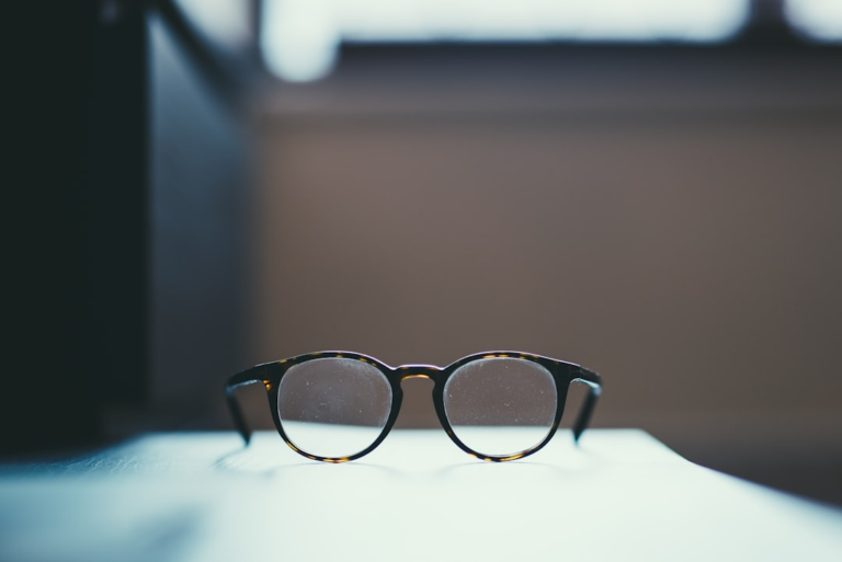 Dusty tortoise-shell eyeglasses rest on a light surface against a muted background, highlighting the importance of clear vision and early detection of eye conditions like AMD.