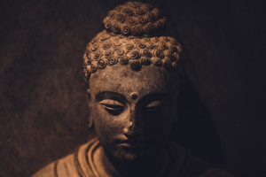 Dark stone Buddha statue with closed eyes and a contemplative expression, softly illuminated against a deep, muted background, embodying the profound peace for meditation, enhanced focus, and creative flow.