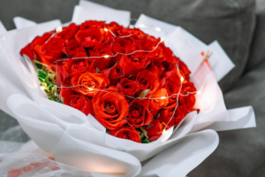 Vibrant red roses arranged in a full bouquet, wrapped in white paper and illuminated by delicate fairy lights, symbolizing natural purity and the pursuit of well-being.