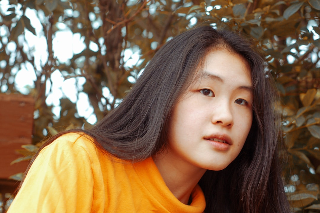 Young woman with long dark hair and an orange top looks thoughtfully, reflecting health and vitality amidst a soft, natural background.