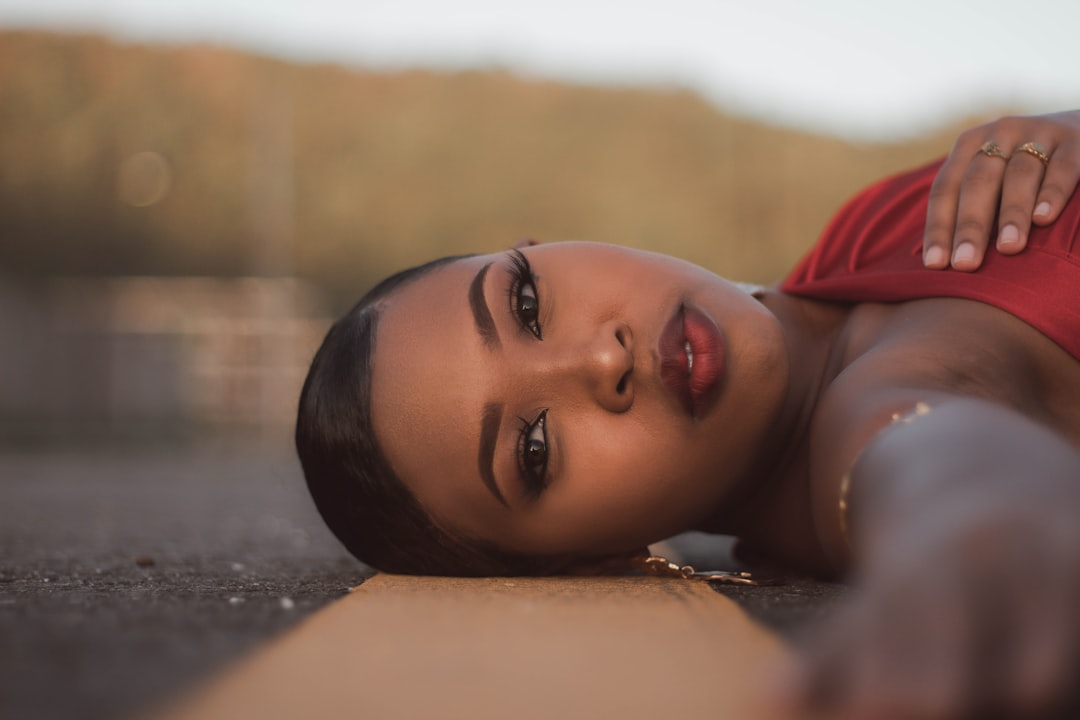 Captivating Black woman with radiant skin and striking makeup lies serenely on a sunlit road, embodying unique beauty through personalized protocols.