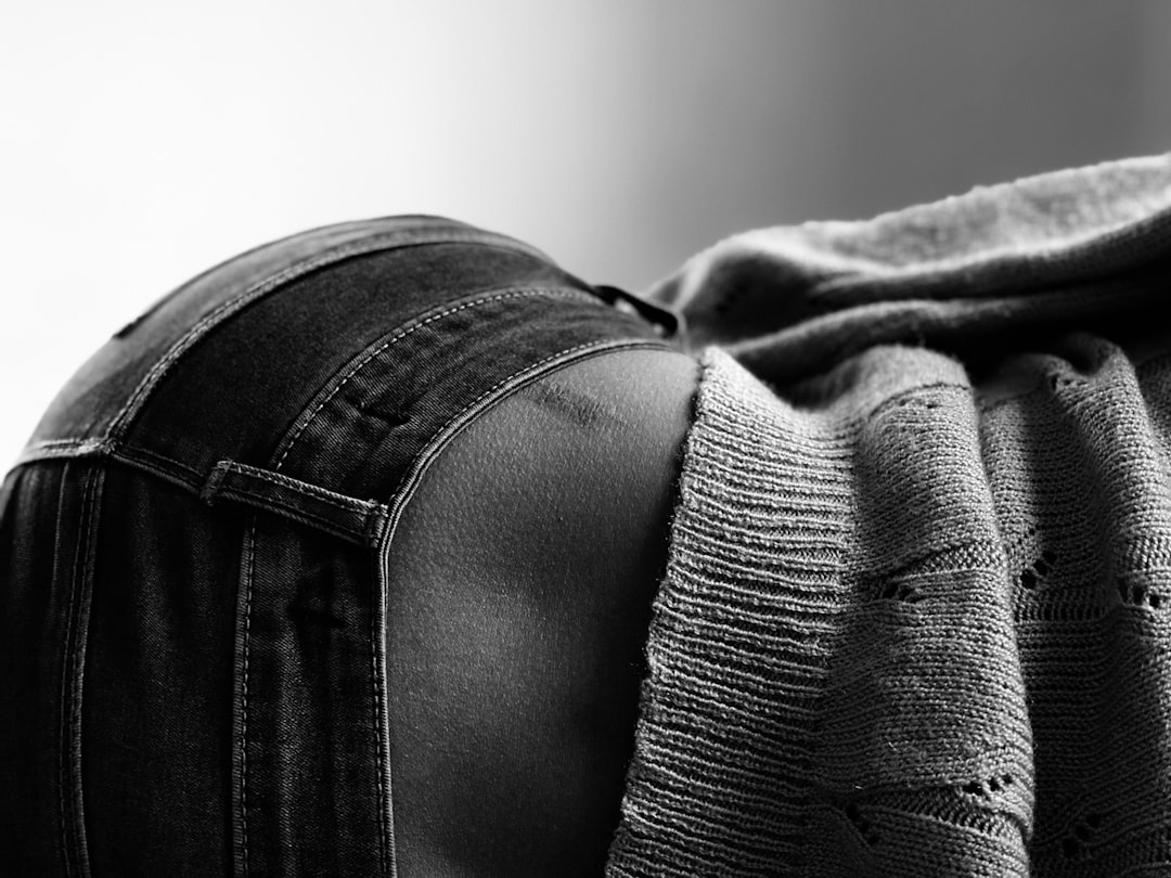 Monochrome close-up showing a person's lower back in dark jeans, gently draped with a textured knitted blanket, evoking a sense of calm and bodily awareness.