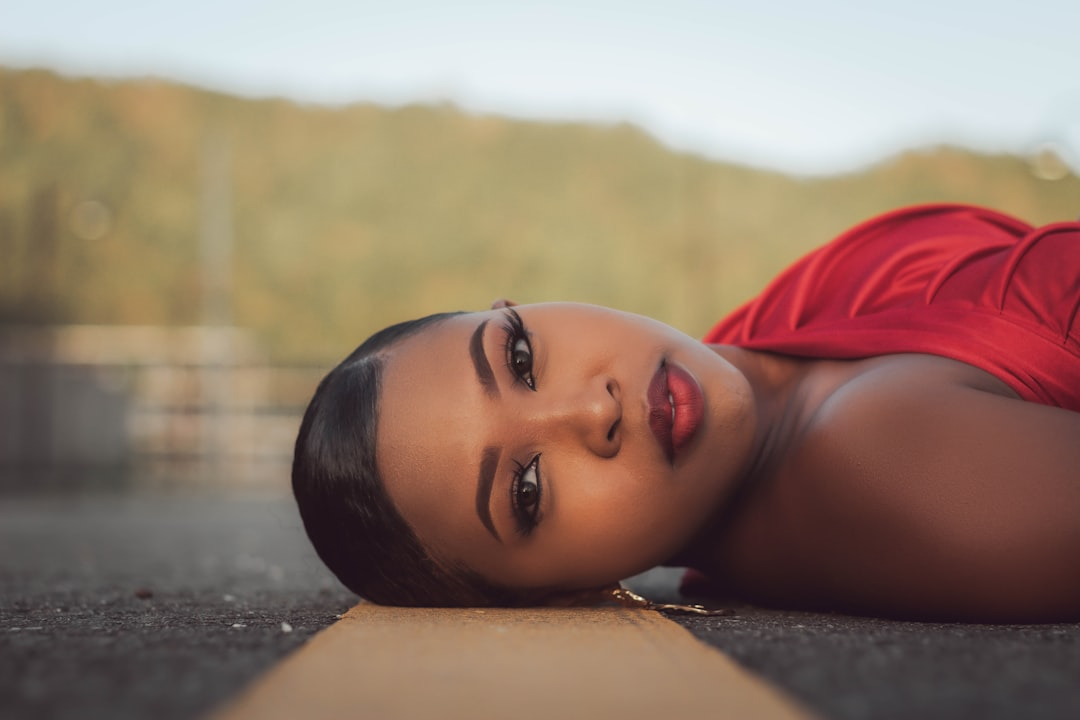 A stunning woman with smooth, radiant skin and a captivating gaze lies serenely on a dark ground with a yellow line, set against a soft, sunlit natural background, embodying healthy skin rejuvenation.