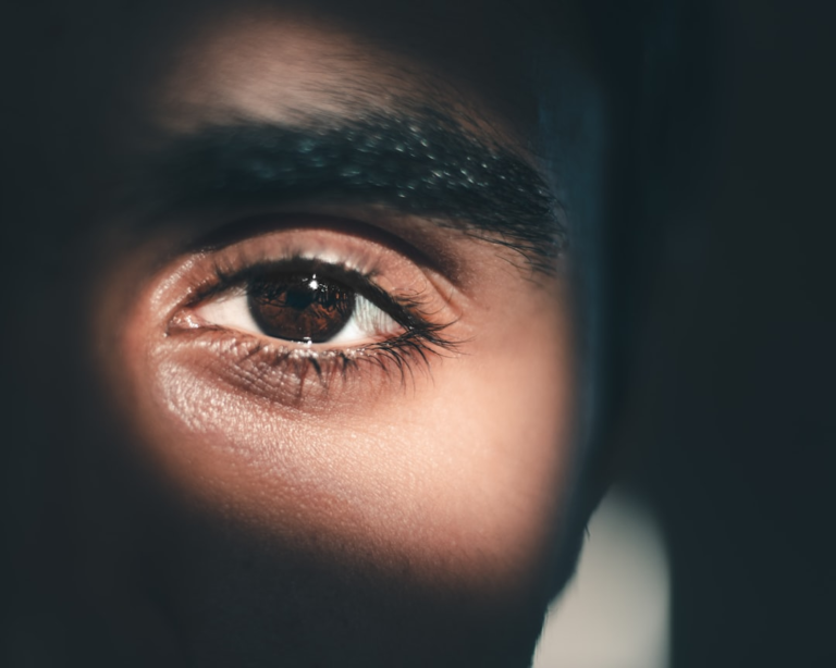 A brown eye is brilliantly illuminated by a focused beam of light against a dark background, symbolizing clarity, hope, and the potential of light therapy for vision.
