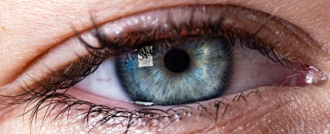 Close-up of a vibrant blue human eye reflecting a grid-patterned light source, illustrating the precise application of light therapy for eye health.