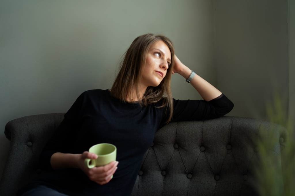 A pensive woman on a gray sofa holds a green mug, contemplating biohacking strategies for digestive well-being and managing conditions like IBS.