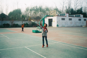 A vibrant young girl in mid-air energetically plays badminton on an outdoor multi-sport court, demonstrating physical activity crucial for mitochondrial health and cellular energy.
