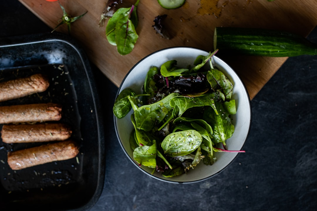 A wholesome meal of vibrant green salad and cooked sausages rests on a dark kitchen counter, symbolizing nourishing choices for mental resilience and longevity.