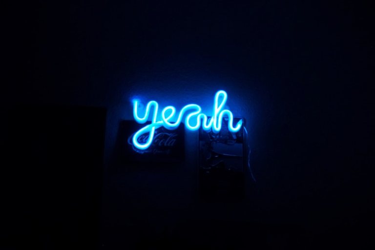 Bright blue neon letters spelling yeah in cursive illuminate a dark space, radiating a feeling of enthusiasm and vitality.