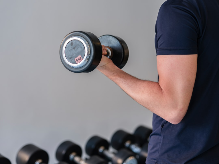 A person's arm performs a bicep curl with an 8kg dumbbell in a clean gym setting, highlighting the role of strength training in boosting metabolism and energy for fat loss.