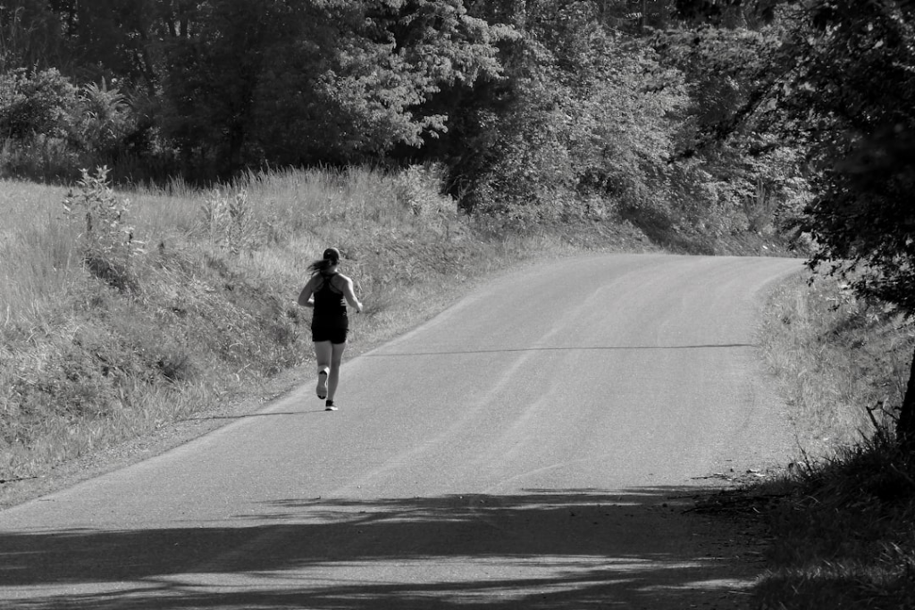 A determined woman runs uphill on a winding paved road through a serene, natural black and white landscape, embodying the pursuit of optimal energy and mitochondrial health.
