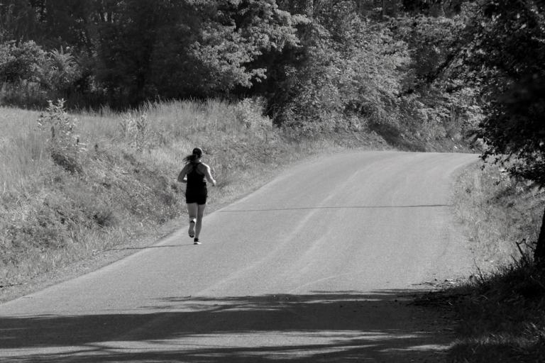 A determined woman runs uphill on a winding paved road through a serene, natural black and white landscape, embodying the pursuit of optimal energy and mitochondrial health.