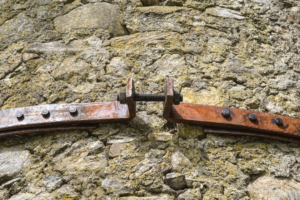 A textured, lichen-covered stone wall features a rusty metal brace tightly secured by a large bolt and nuts, symbolizing enduring strength and structural optimization.