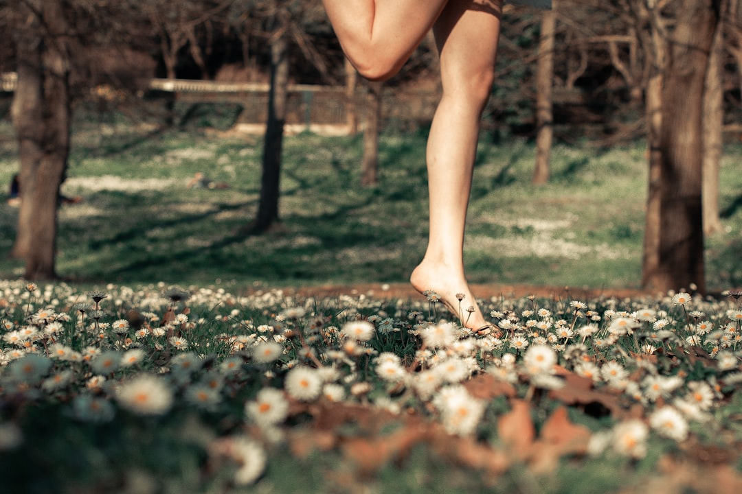 Bare legs and a foot gently step across a vibrant meadow of white daisies and green grass, symbolizing a natural, grounding approach to personalized gut biohacking and optimal digestion.