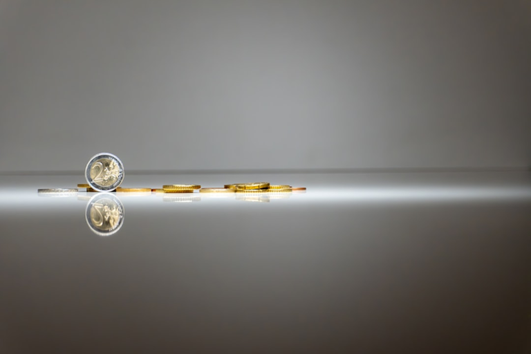 A prominent 2 Euro coin stands upright on a highly reflective surface, with other Euro coins behind it, illuminated by a bright horizontal light against a minimalist grey background, conveying a sense of precise, personalized investment.