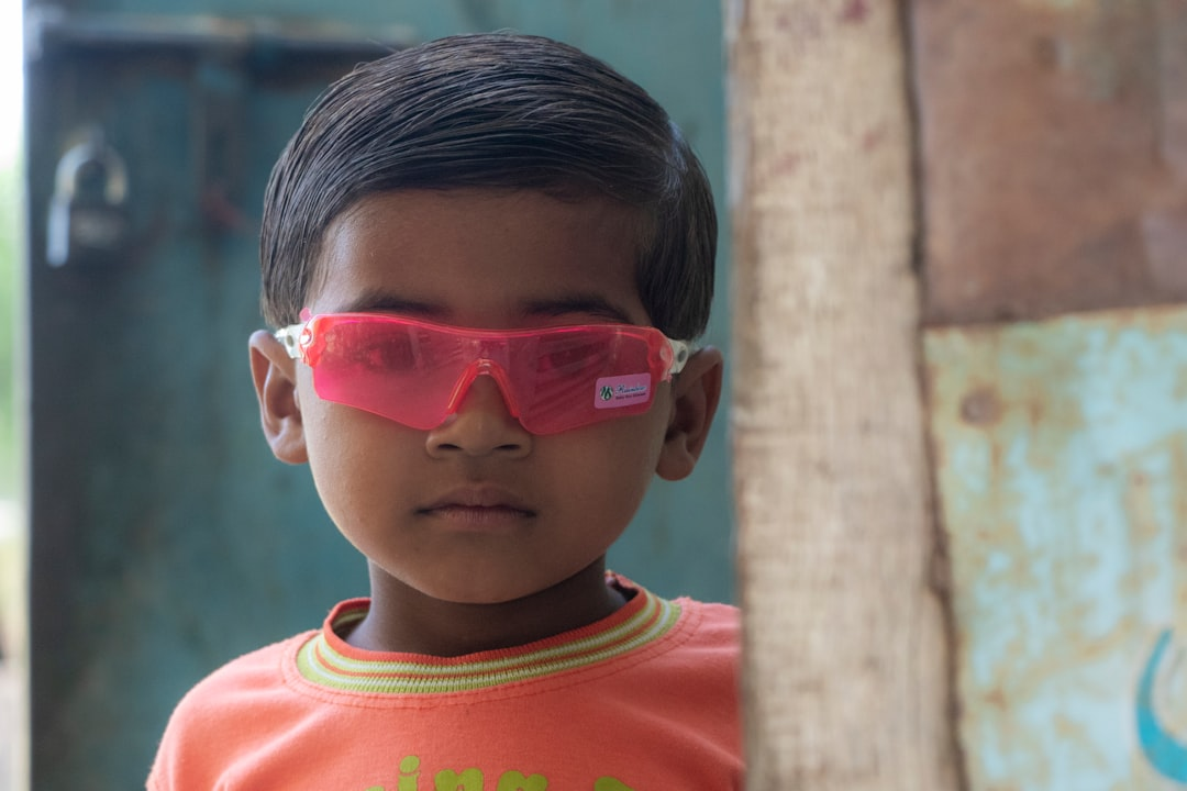 A young child wearing vibrant pink protective sunglasses looks directly forward, symbolizing crucial blue light and UV eye safety for children.