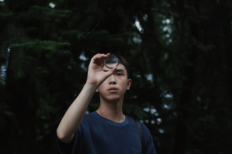 Focused young person gazes thoughtfully through a dark lens filter, symbolizing improved clarity and protection for eye health and ocular longevity against a natural green backdrop.