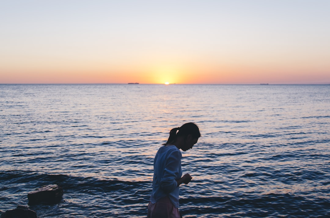 A contemplative woman stands by the tranquil ocean at sunset, reflecting a sense of peace and calm essential for stress management.