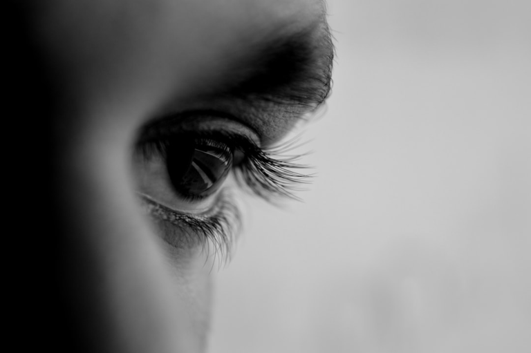 Detailed black and white close-up of a human eye with long eyelashes, highlighting vision and the focus required for myopia (nearsightedness) correction exercises.