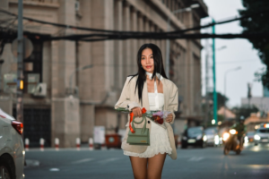 Stylish young woman with long, glossy dark hair and a confident expression stands on a city street, wearing a white mini-skirt and beige blazer, exemplifying optimal hair health and vibrant growth.