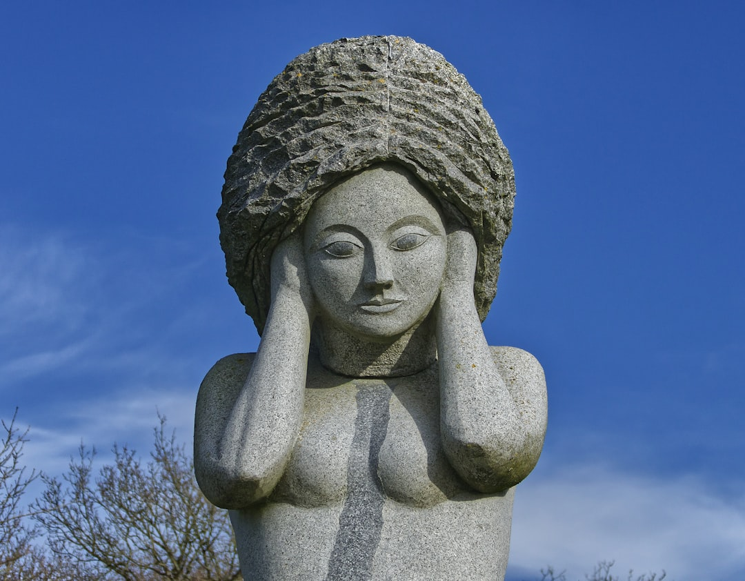 Granite sculpture of a woman holding her hands to her head with closed eyes against a clear blue sky, symbolizing the physical and mental burden of stress.