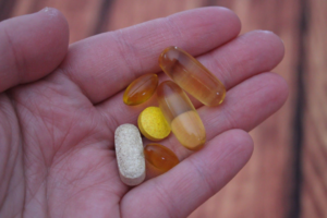 A hand holds a variety of health supplements, including clear softgel capsules and a tablet, emphasizing the role of nutritional support in holistic wellness for the gut-eye-brain axis, sleep, and vision.