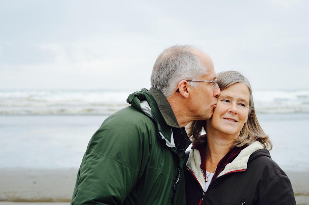 An affectionate older couple embraces on a serene beach under an overcast sky, symbolizing the joy of a long healthspan.