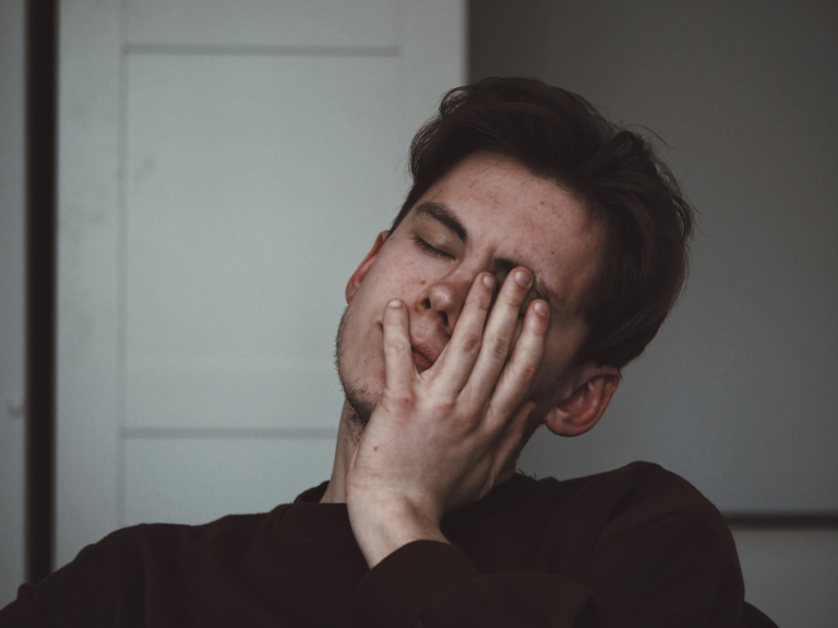 A young person rubs their tired, closed eyes with a hand, conveying the eye strain and fatigue often linked to blue light and EMF exposure, which can impact ocular health.