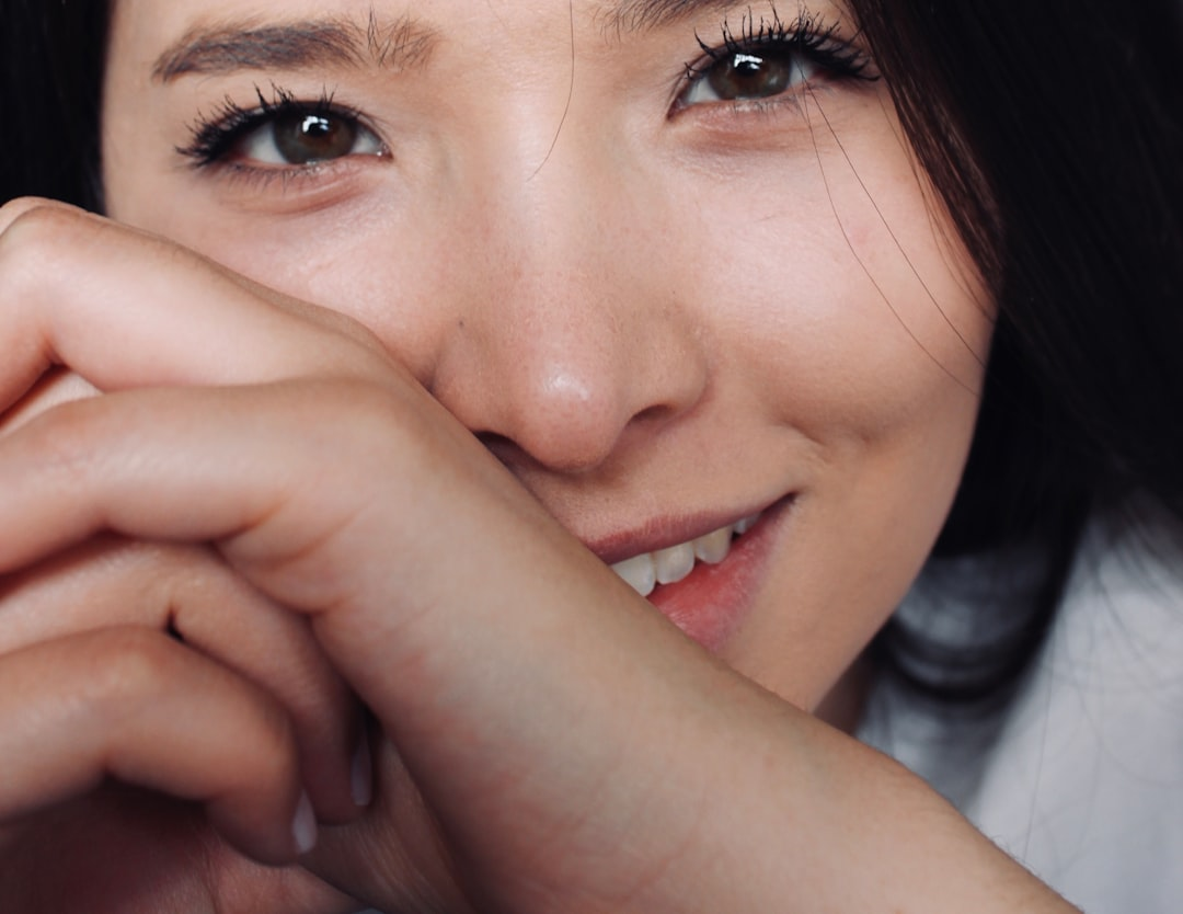 Close-up of a young woman with bright, clear eyes and a gentle, hand-covered smile, conveying the importance of healthy vision and well-being.