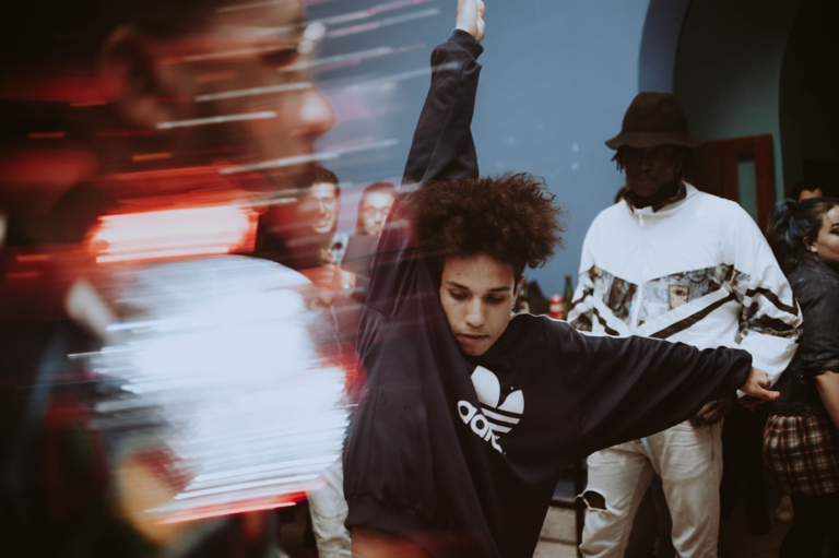 Young person with curly hair in an Adidas sweatshirt displaying powerful, focused movement in a dynamic, dimly lit setting, reflecting the vibrant energy of cellular powerhouses.