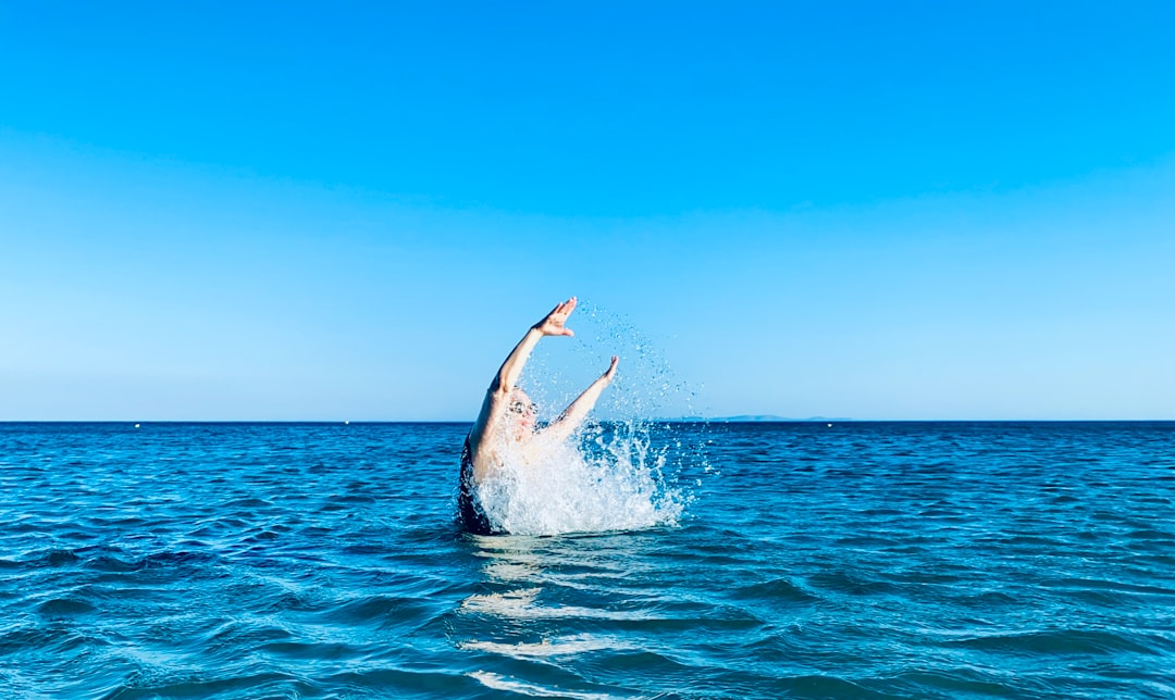 A person joyfully emerges from the clear blue ocean with a splash, bathed in bright natural light under a vast sky, embodying vitality for circadian health.