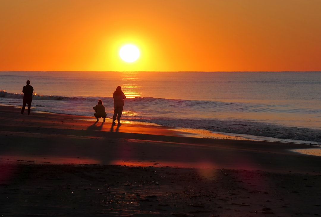 Three silhouetted figures stand on a beach at a brilliant orange sunrise, with the sun's reflection shimmering on the ocean, evoking a sense of renewal and optimized energy.