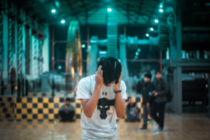 A young person covers their ears in a vast, dimly lit industrial space with teal lighting, conveying the struggle with mental overwhelm or difficulty concentrating often addressed by nootropics.