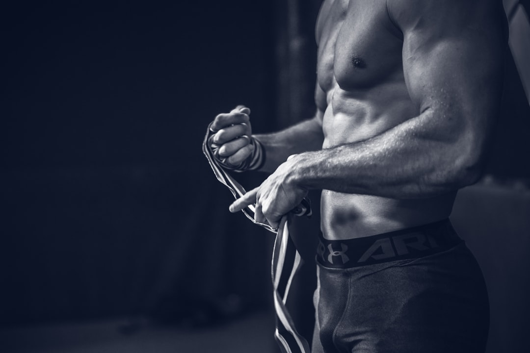 Muscular athlete with defined abs and biceps intently wrapping their hands in a stark black and white gym scene, symbolizing the strength and health achieved through optimal nutrient absorption.