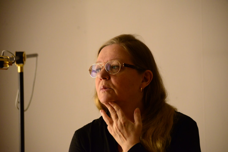 Pensive woman wearing gold-rimmed daily eyewear, her lenses subtly reflecting light as she considers the importance of UV protection, in a setting with specialized equipment.