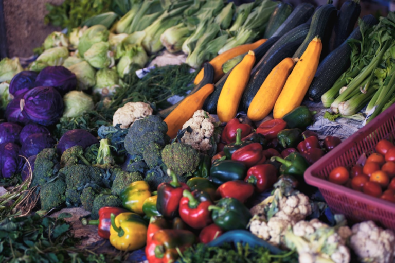 A vibrant array of fresh, colorful vegetables including purple cabbage, broccoli, bell peppers, and squash, are abundantly displayed at a market, promoting healthy ingredients for vision-boosting recipes and improved eye health.
