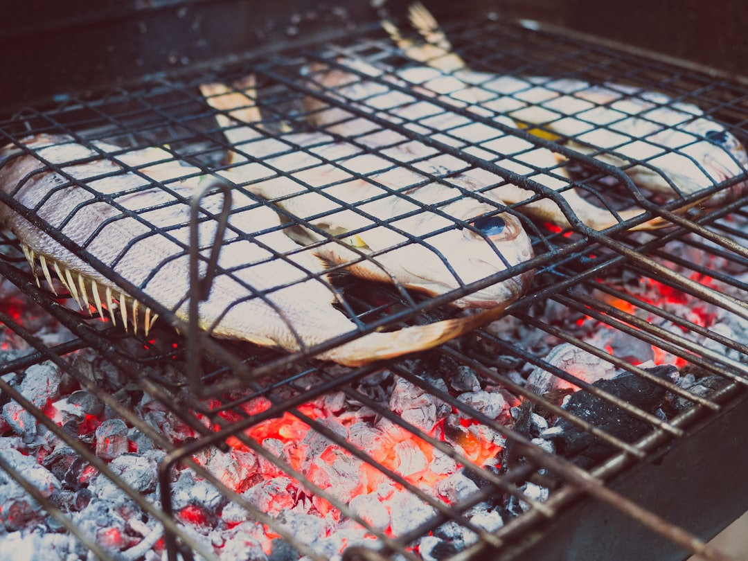 Fresh whole fish cook over vibrant red hot charcoal embers on a wire barbecue grill.
