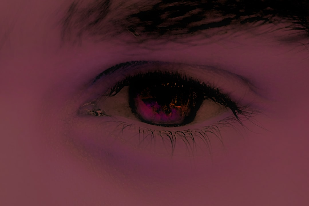 A human eye with a reddish-purple tint reflects glowing digital lights, symbolizing the potential strain and impact of blue light on eye health and sleep.